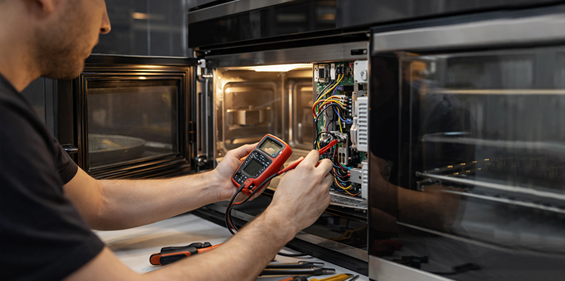 Technician diagnosing microwave with multimeter — KTech Appliance Services Perth